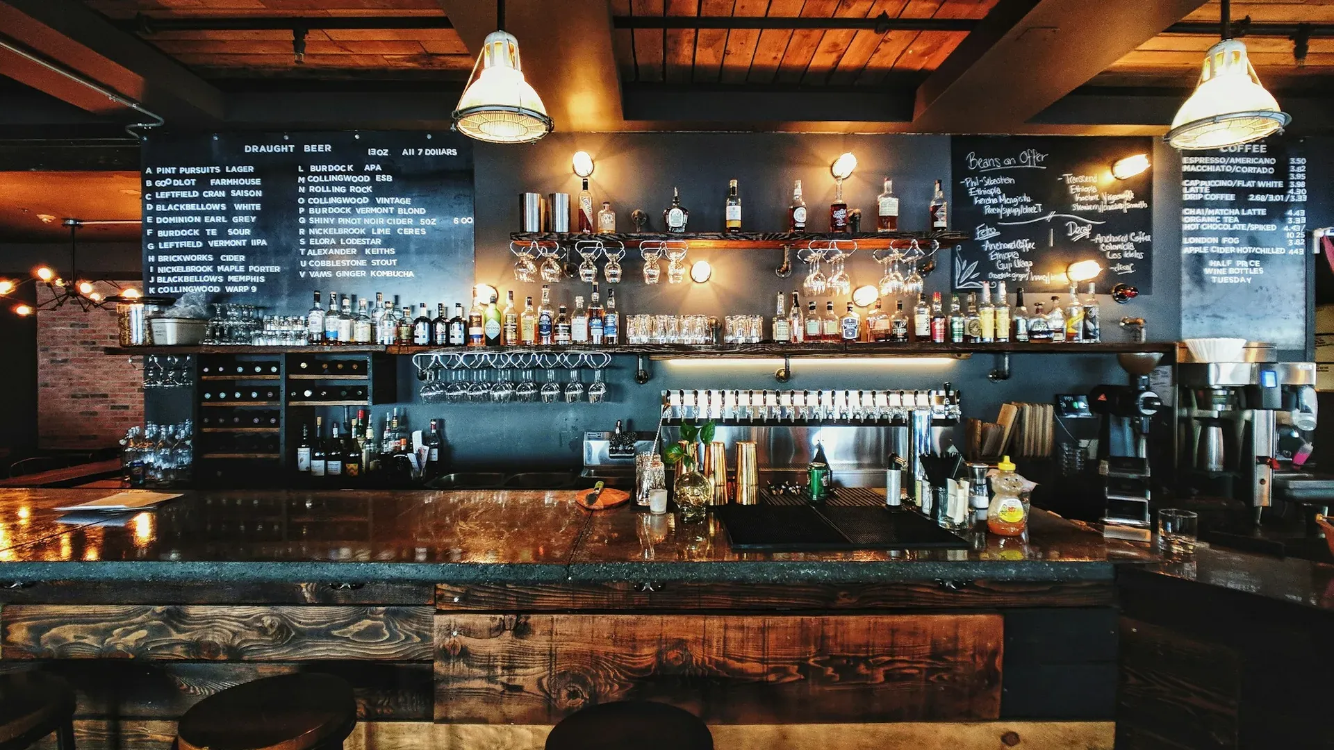 Bar mit beschriebener Kreidetafel, Barhockern und Pendelleuchten am Abend