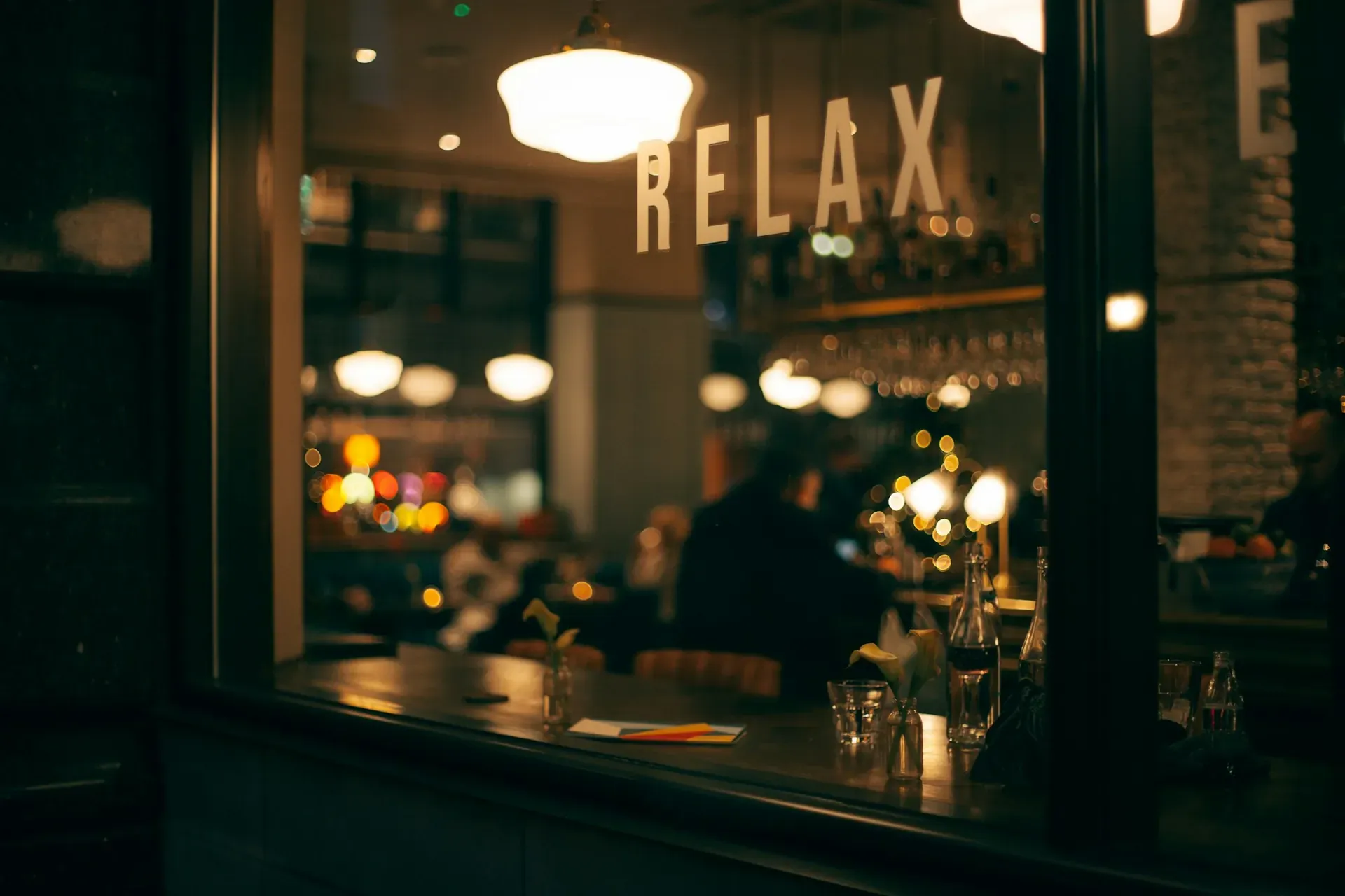 Blick durch die Scheibe in eine abendlich beleuchtete Bar mit Leuchtschrift und Kerzenlicht