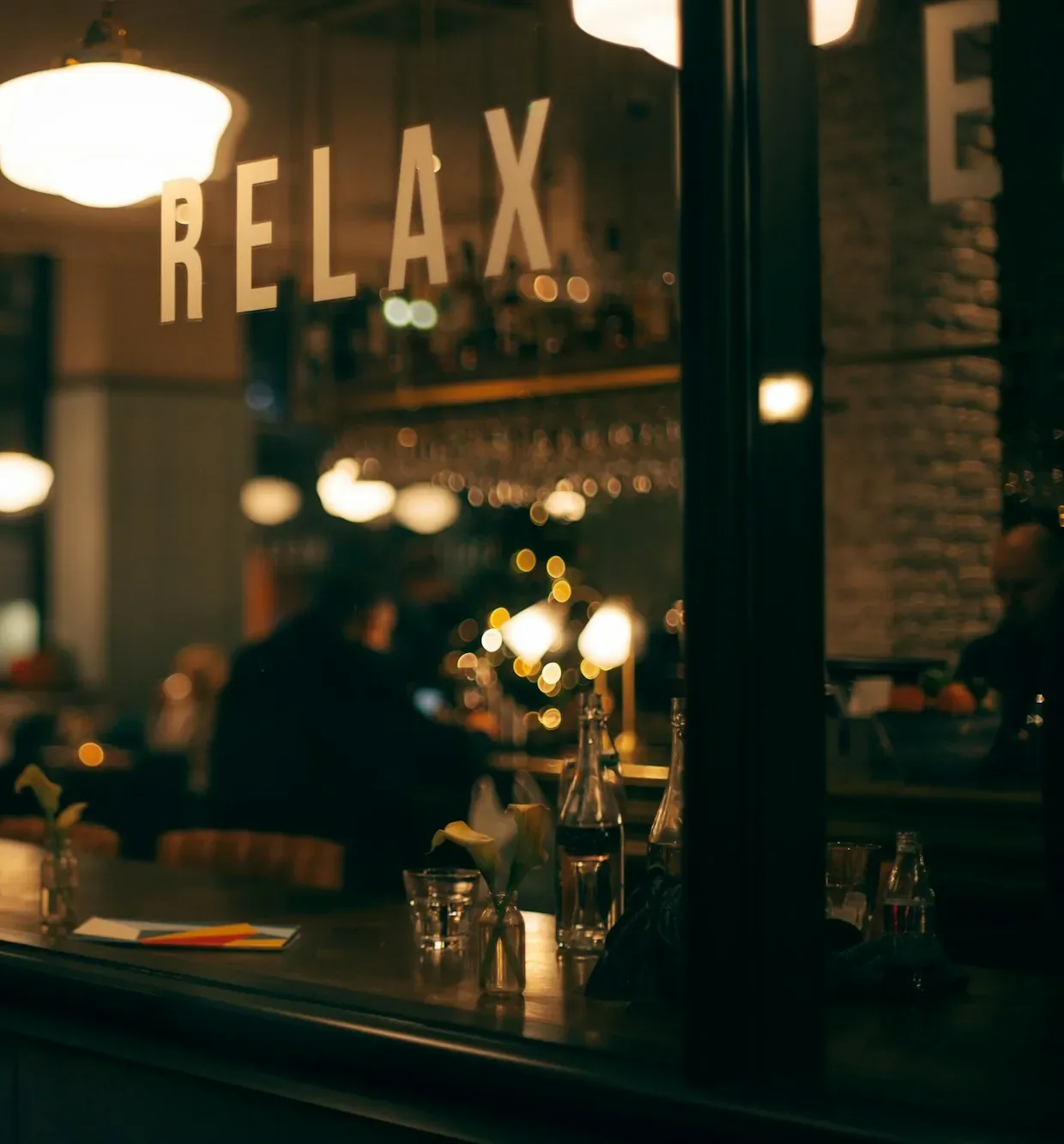 Nächtliche Bar hinter Glas mit Leuchtschrift „Relax" und Kerzenlicht