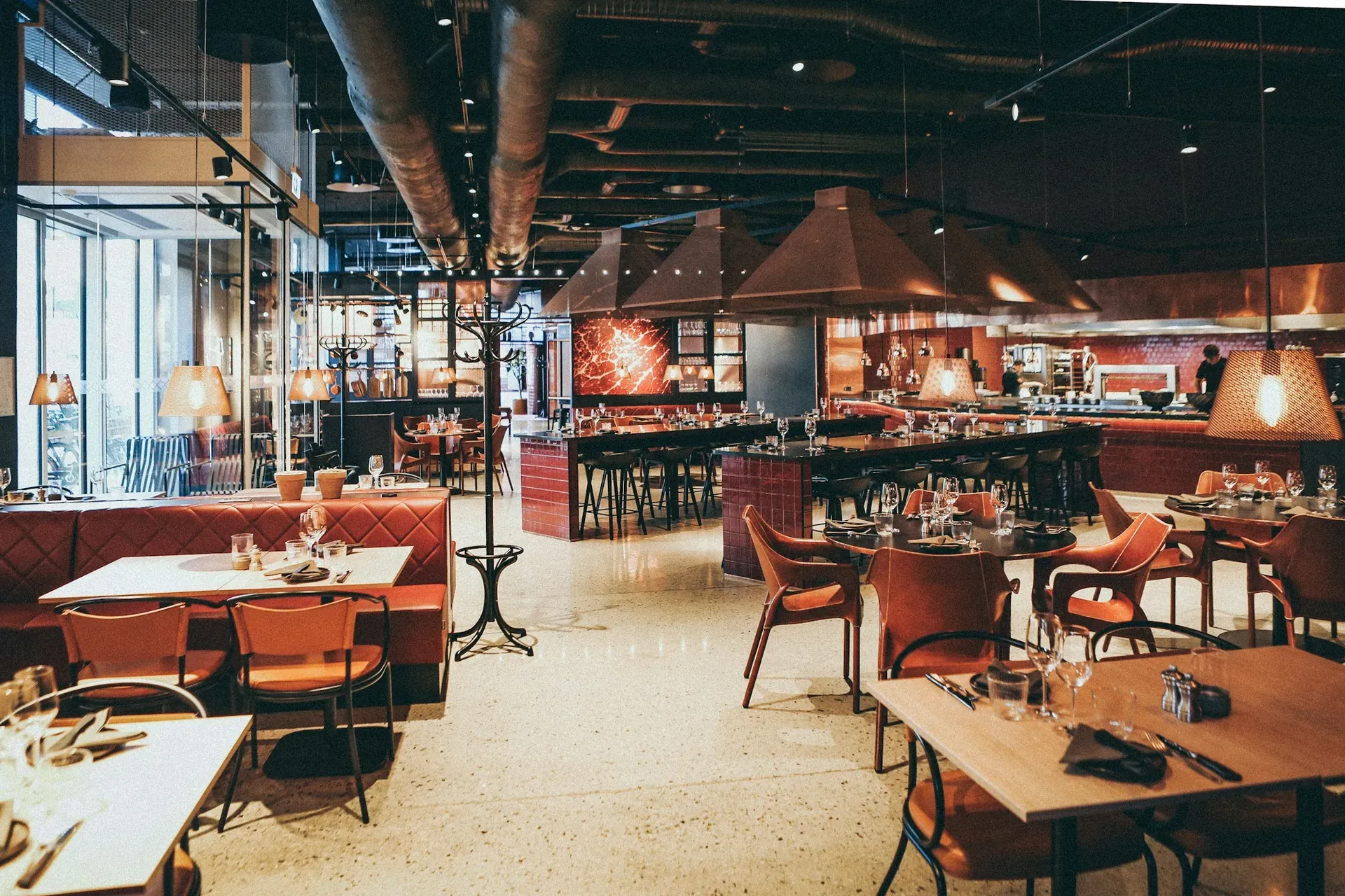 Leerer Restaurantraum mit Holztischen, Ledersesseln und warmen Pendelleuchten