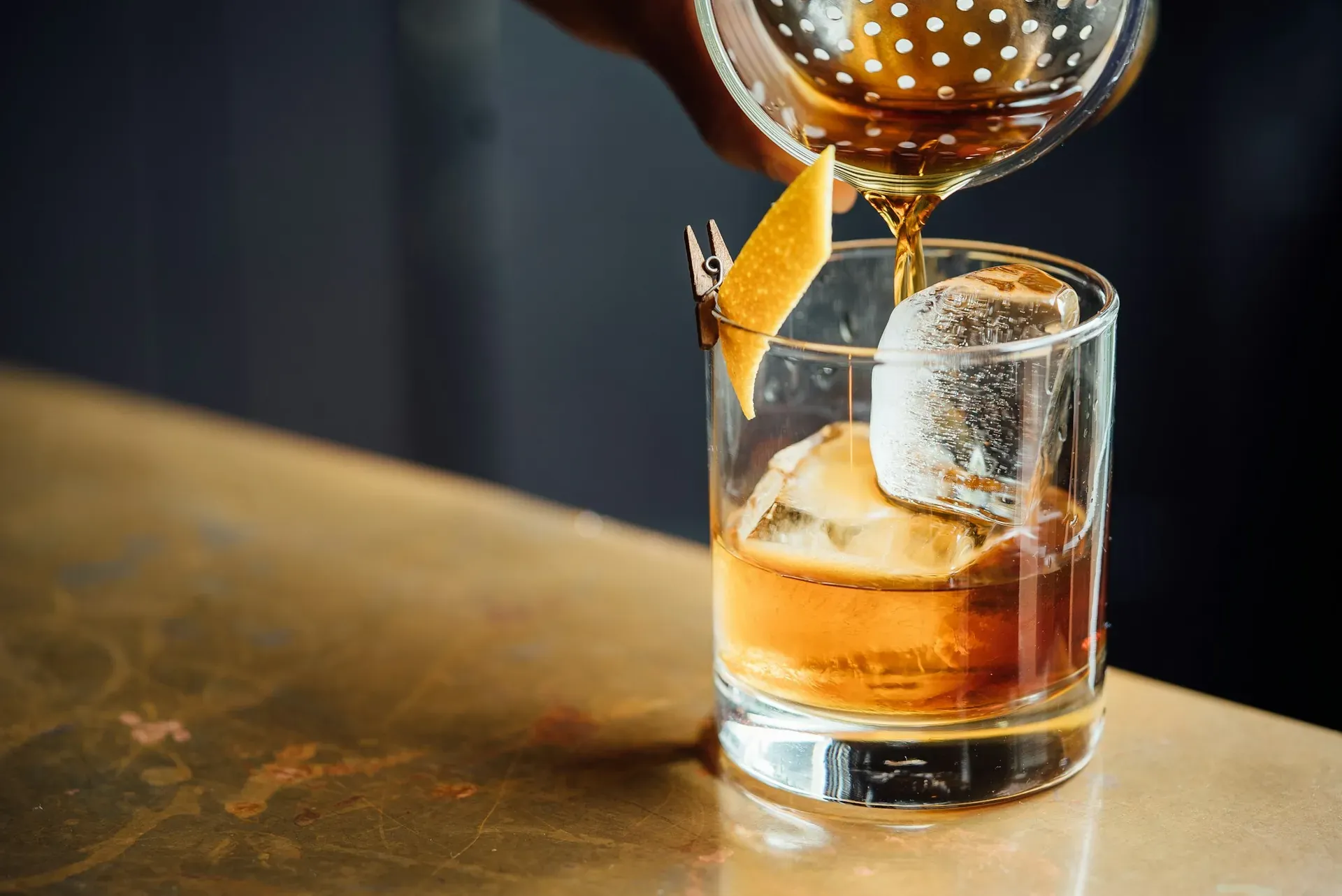 Barkeeper gießt einen Cocktail über einen großen Eiswürfel in ein Glas