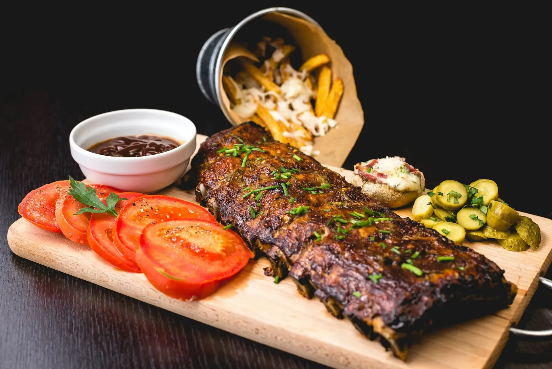 Holzbrett mit gegrillten Rippchen, Tomaten, Röstkartoffeln und Dip